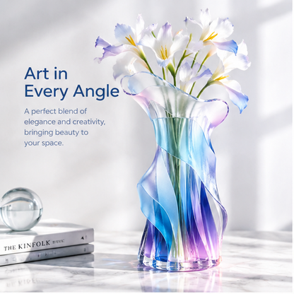 PLIOXOO® crystal glass ruffled vase with white calla lilies on white surface in natural window light – full product beauty shot showing sinuous glass fins spiraling from pink base through cobalt blue to violet ruffled rim